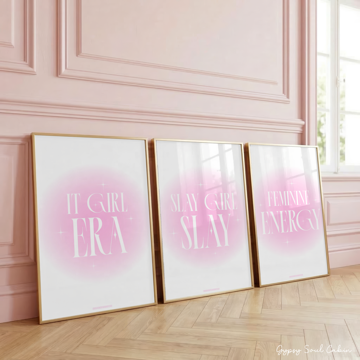 Three pink gradient aura wall art prints in gold frames leaning against a classic panelled pink wall, featuring typography for It Girl Era, Slay Girl Slay, and Feminine Energy.