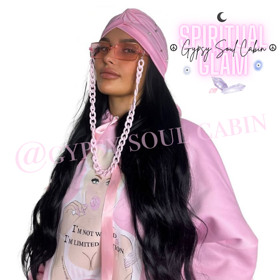 Close-up of a woman wearing a pink hoodie with a graphic of a woman holding a lollipop and the text 'I'm not weird, I'm limited edition,' accessorised with pink fashion sunglasses, and a matching pink bohemian gypsy headscarf, against a white background.
