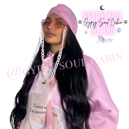 Close-up of a woman wearing a pink hoodie with a graphic of a woman holding a lollipop and the text 'I'm not weird, I'm limited edition,' accessorised with pink fashion sunglasses, and a matching pink bohemian gypsy headscarf, against a white background.