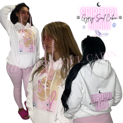 Back view of a white oversized hoodie featuring a pink "Spiritual Glam" logo, a small moon graphic, and "Gypsy Soul Cabin" text, worn by a woman with long black hair, with a similar hoodie worn by the woman with a graphic on the front.