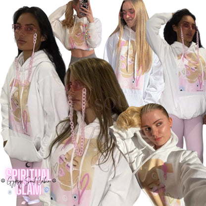 A collage of images showing a white oversized hoodie with front pocket and tie pull strings, featuring pink and purple spiritual-themed graphics and text on the front and back.