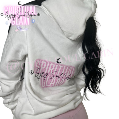 Close-up of a white oversized hoodie featuring colourful spiritual girl artwork, "Spiritual Glam" text in pink, peace symbols, and "Gypsy Soul Cabin" signature, worn by a woman with long black hair.