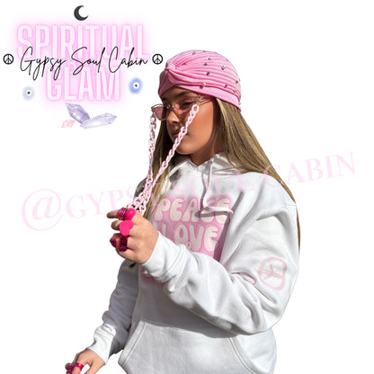 Side profile view of a model showcasing chunky pink Y2K rings, a pink sunglasses chain lanyard, a pleated turban, and a white Peace Love and Humble slogan hoodie by Gypsy Soul Cabin.