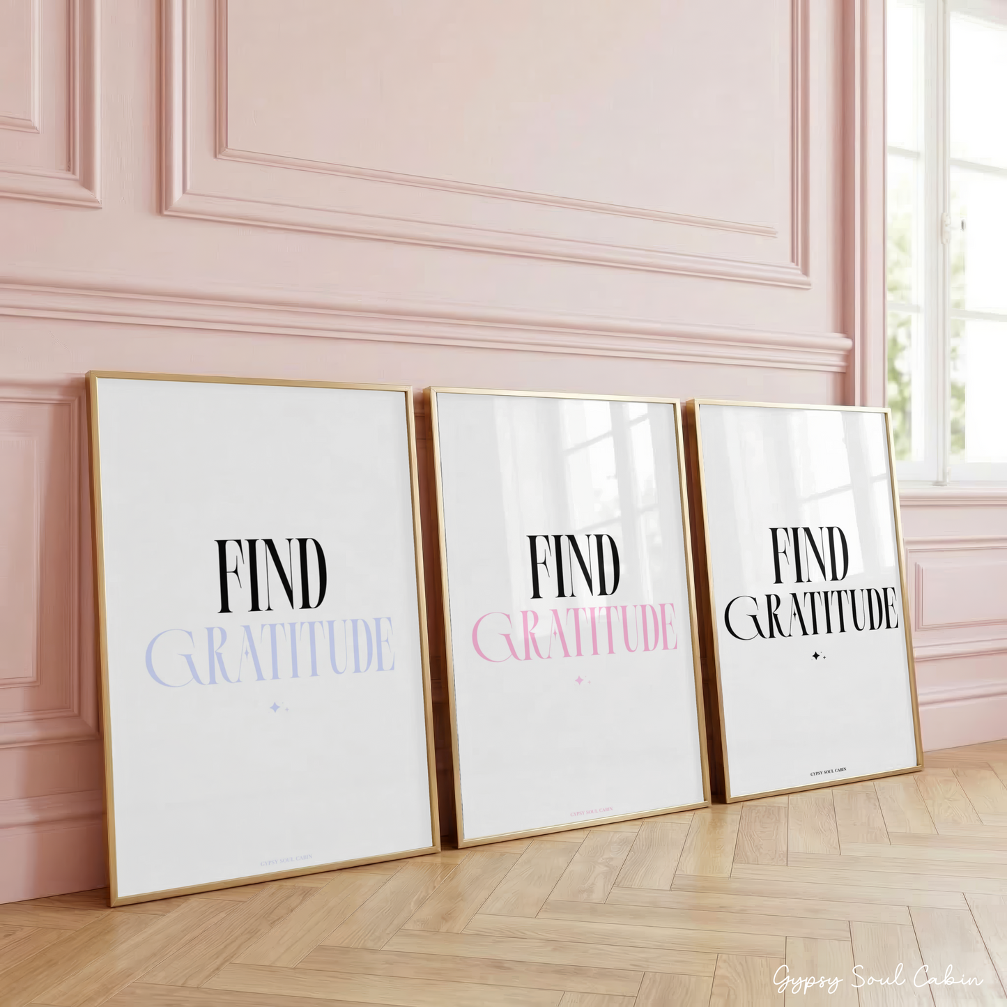 Three minimalist typography prints reading Find Gratitude in blue-lilac, pastel pink, and classic black text fonts, displayed in gold frames leaning against a classic panelled pink wall.