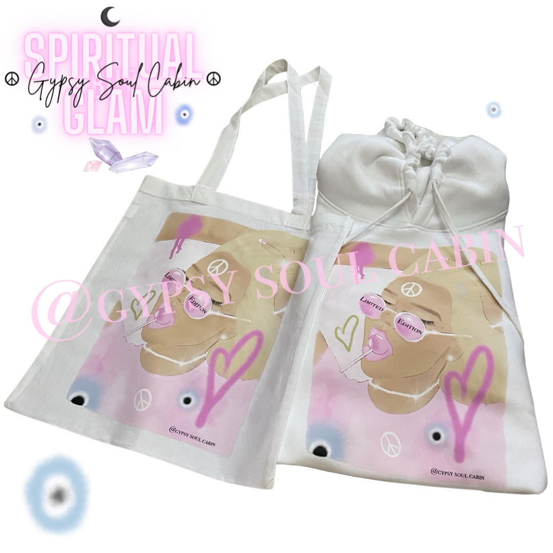 A white canvas tote bag styled next to a matching white Gypsy Soul Cabin hoodie, both featuring the same limited edition female artwork with a pink lollipop.