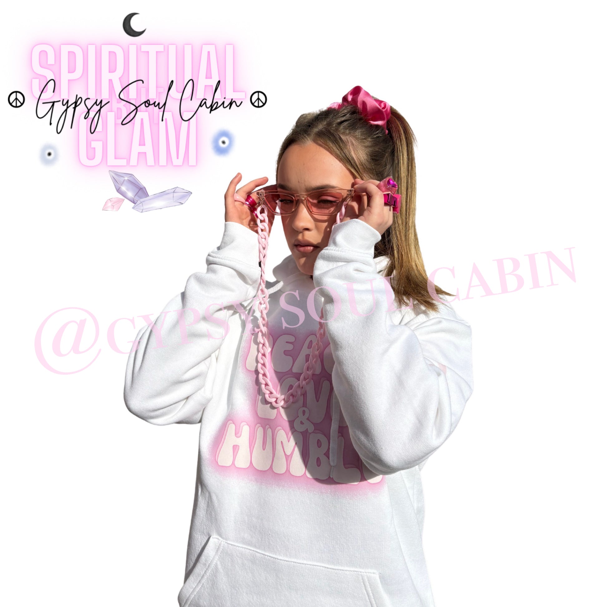 Model adjusting pink sunglasses while showcasing chunky pink Y2K rings, a matching pink hair scrunchie, a chain lanyard, and a white Peace Love Humble graphic hoodie by Gypsy Soul Cabin.